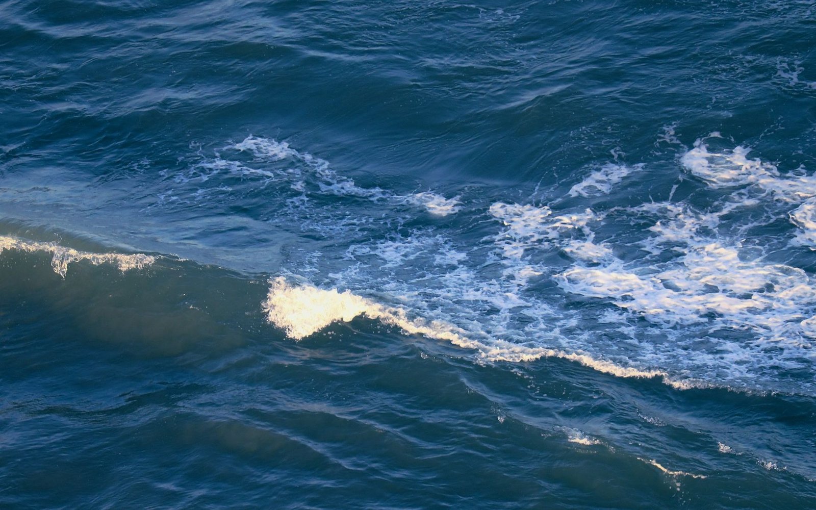 Deep blue ocean with a breaking wave, seen from above